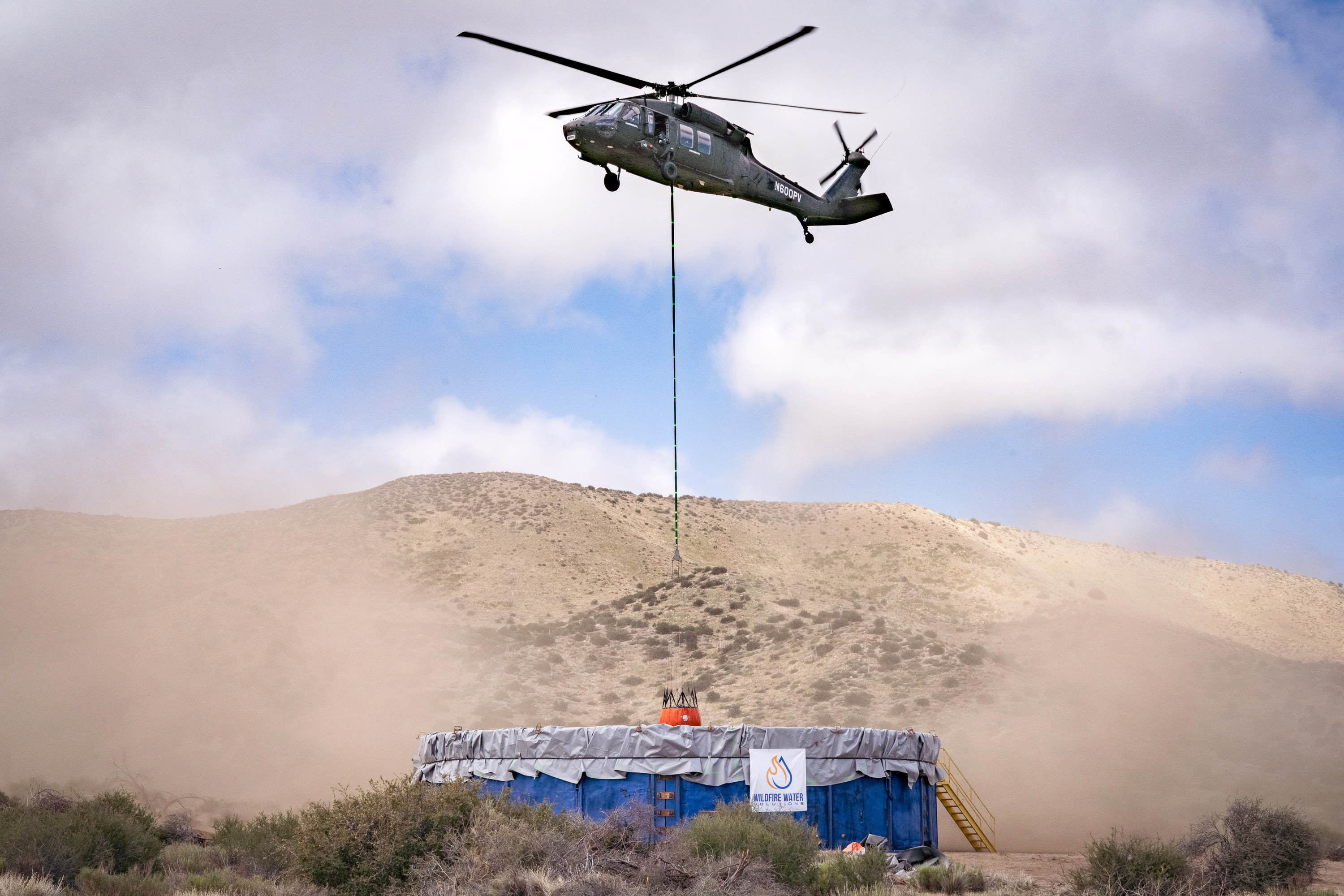Un helicóptero Black Hawk en picado, cargando agua en un contenedor, foto Lockheed Martin